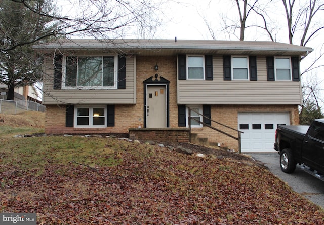 raised ranch featuring brick siding, an attached garage, driveway, and fence