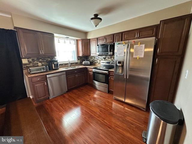 kitchen featuring dark wood finished floors, decorative backsplash, appliances with stainless steel finishes, and a sink