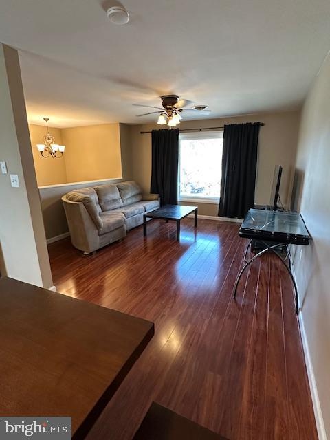 living room featuring baseboards, wood finished floors, and ceiling fan with notable chandelier