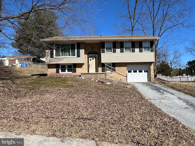 raised ranch with a garage, fence, brick siding, and driveway