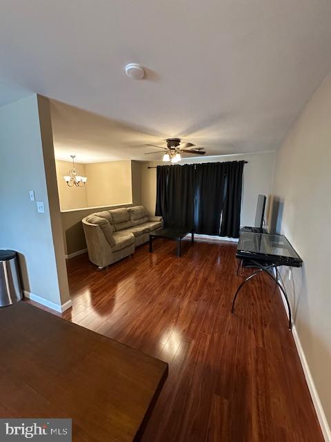 unfurnished living room with ceiling fan with notable chandelier, wood finished floors, and baseboards