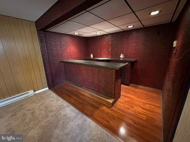 bar with light wood-style flooring, a paneled ceiling, baseboard heating, and a dry bar