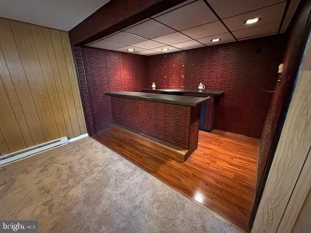 bar with wooden walls, a drop ceiling, a bar, light colored carpet, and light wood-type flooring