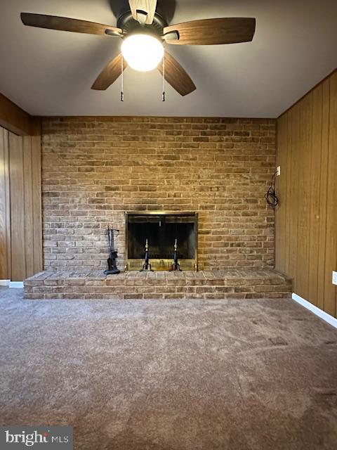 unfurnished living room featuring brick wall, a fireplace, ceiling fan, wood walls, and carpet flooring