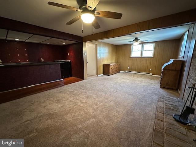 interior space with wood walls, a baseboard heating unit, a ceiling fan, and carpet floors