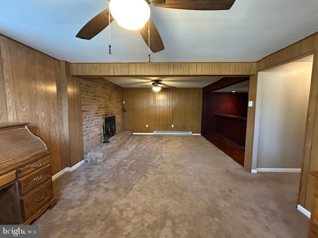 unfurnished living room with a brick fireplace, wooden walls, a ceiling fan, and carpet floors