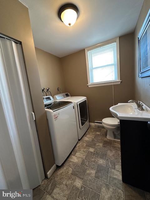 clothes washing area with baseboards, laundry area, separate washer and dryer, stone finish floor, and a sink