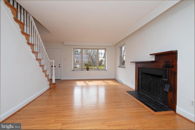 unfurnished living room featuring stairway, baseboards, wood finished floors, and a tiled fireplace