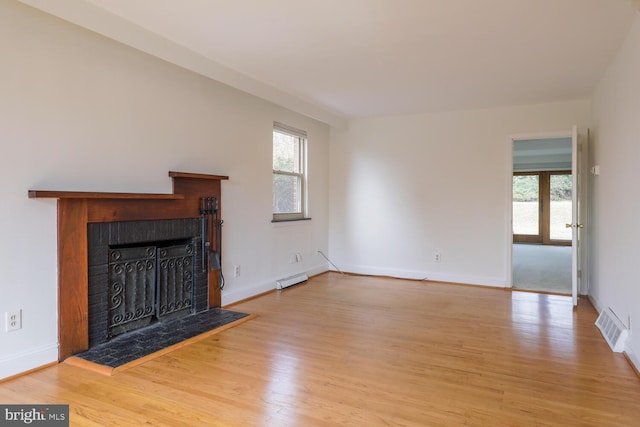 unfurnished living room featuring a tiled fireplace, visible vents, a healthy amount of sunlight, and wood finished floors