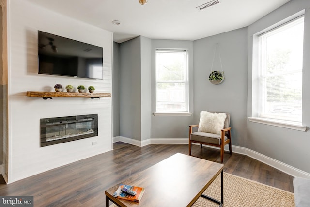 living area featuring wood finished floors, a glass covered fireplace, visible vents, and baseboards