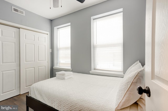 bedroom with dark wood-type flooring, a closet, visible vents, and a ceiling fan