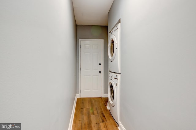 clothes washing area featuring light wood-style floors, stacked washer and clothes dryer, baseboards, and laundry area