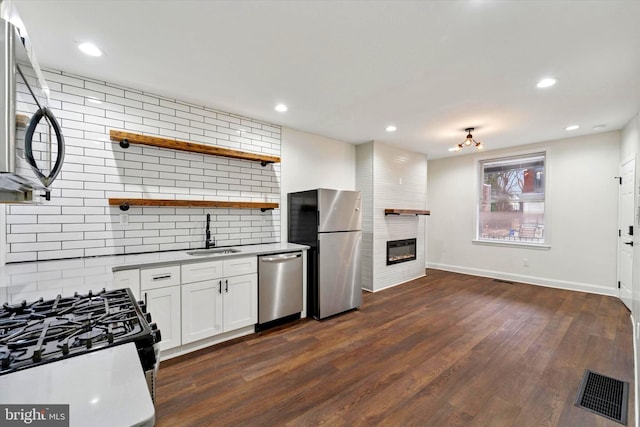 kitchen with a large fireplace, visible vents, dark wood-type flooring, stainless steel appliances, and a sink