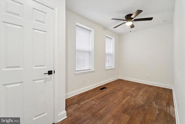 unfurnished room featuring dark wood-style floors, visible vents, baseboards, and a ceiling fan