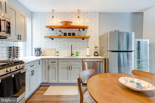 kitchen with light countertops, light wood-style flooring, decorative backsplash, appliances with stainless steel finishes, and a sink