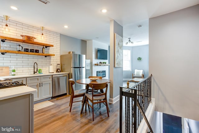 kitchen with a sink, stainless steel appliances, light wood finished floors, and backsplash