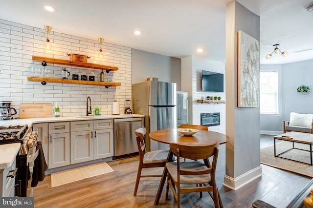 kitchen featuring decorative backsplash, light wood-style flooring, stainless steel appliances, light countertops, and a sink