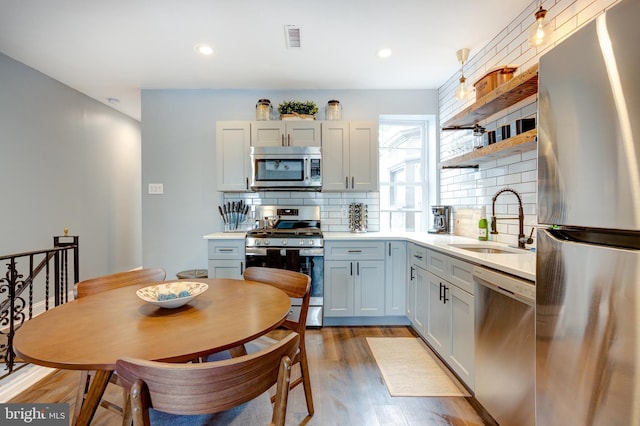 kitchen with stainless steel appliances, a sink, visible vents, open shelves, and light wood finished floors