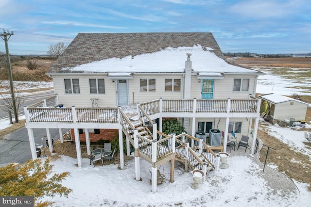 snow covered rear of property with stairway, cooling unit, a deck, and roof with shingles