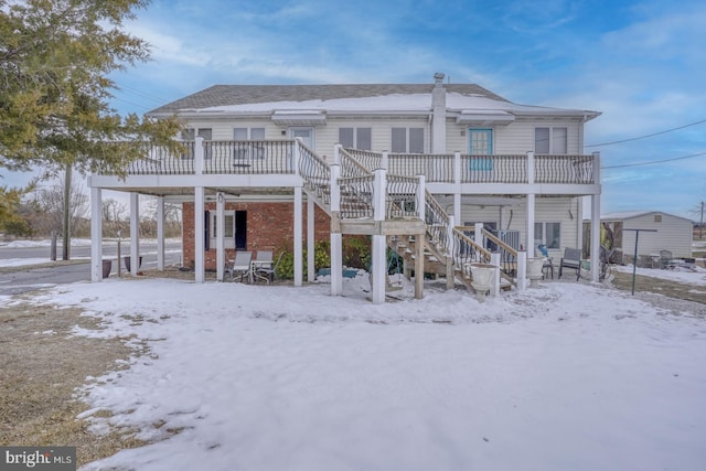 snow covered rear of property with a deck, stairs, and a shingled roof