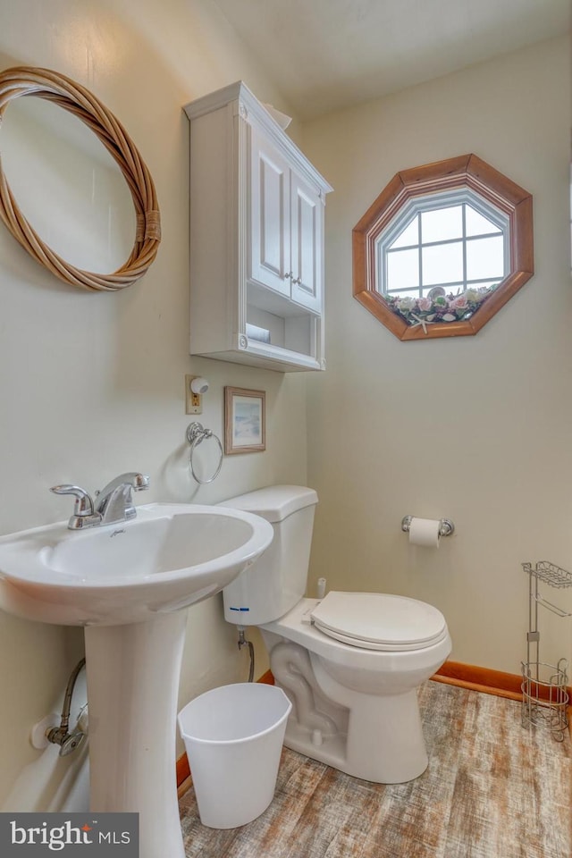 half bathroom featuring a sink, baseboards, toilet, and wood finished floors