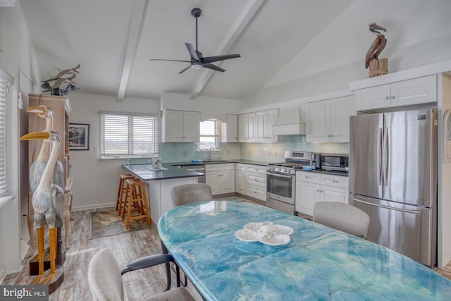 kitchen featuring dark countertops, vaulted ceiling with beams, premium range hood, decorative backsplash, and appliances with stainless steel finishes