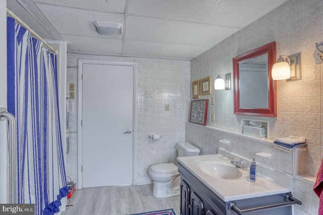 full bathroom with a shower with curtain, toilet, wood finished floors, tile walls, and vanity