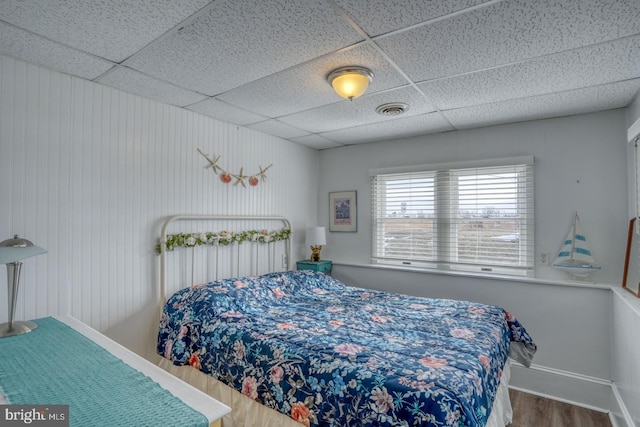 bedroom with baseboards, wood finished floors, visible vents, and a paneled ceiling