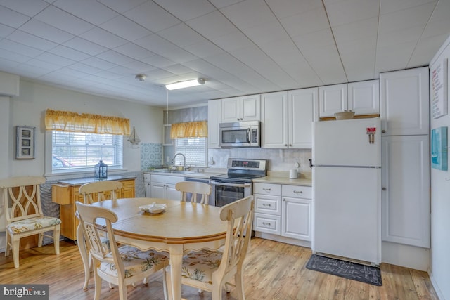 kitchen with a sink, stainless steel appliances, white cabinets, light wood finished floors, and light countertops