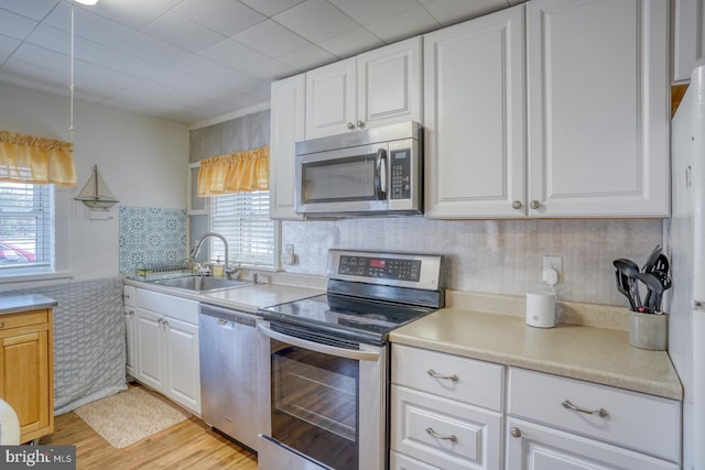 kitchen with white cabinets, appliances with stainless steel finishes, light wood-type flooring, and a sink