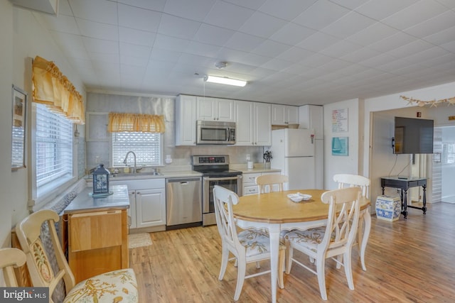 kitchen featuring light wood finished floors, light countertops, stainless steel appliances, white cabinetry, and a sink