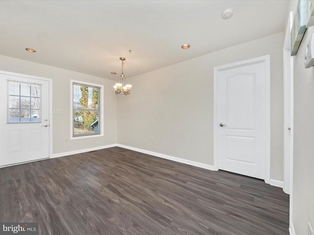 unfurnished dining area featuring dark wood-style floors, a notable chandelier, and baseboards