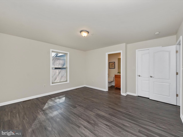 unfurnished bedroom with ensuite bathroom, dark wood-style flooring, visible vents, and baseboards