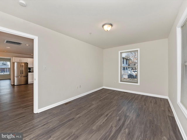 empty room with baseboards, visible vents, and dark wood-type flooring