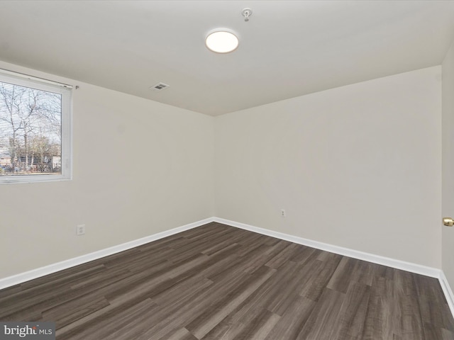 spare room featuring baseboards, visible vents, and dark wood-type flooring