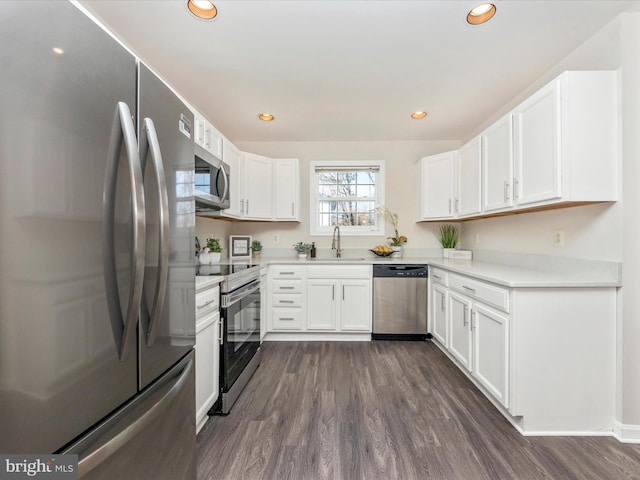 kitchen featuring appliances with stainless steel finishes, dark wood-type flooring, white cabinetry, a sink, and recessed lighting