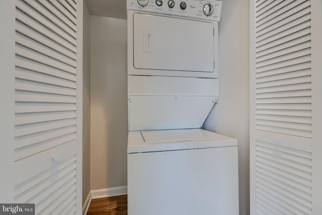 clothes washing area with baseboards, stacked washer and clothes dryer, dark wood-style floors, and laundry area