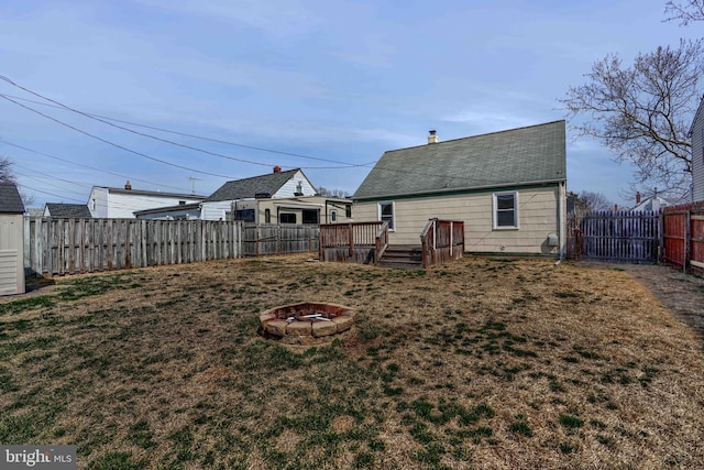 rear view of house featuring a yard, a fire pit, a fenced backyard, and a wooden deck