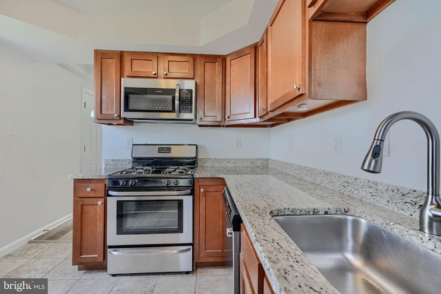 kitchen featuring light stone counters, brown cabinets, stainless steel appliances, and a sink