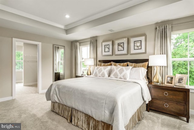 bedroom with light colored carpet, a tray ceiling, multiple windows, and baseboards