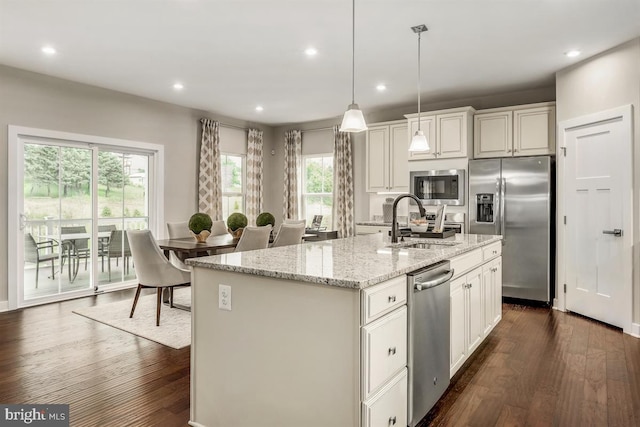 kitchen with appliances with stainless steel finishes, dark wood-type flooring, a sink, and light stone counters