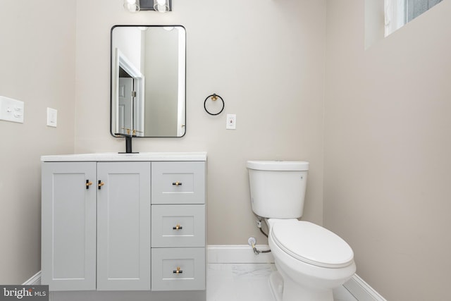 bathroom featuring toilet, marble finish floor, baseboards, and vanity