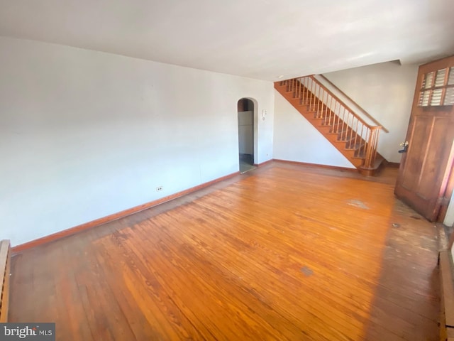 unfurnished living room featuring arched walkways, stairway, wood finished floors, and baseboards