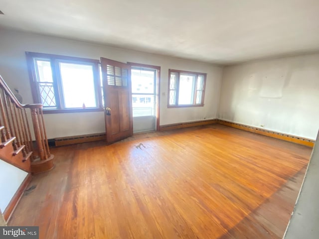 unfurnished living room with a baseboard heating unit, plenty of natural light, stairway, and wood finished floors