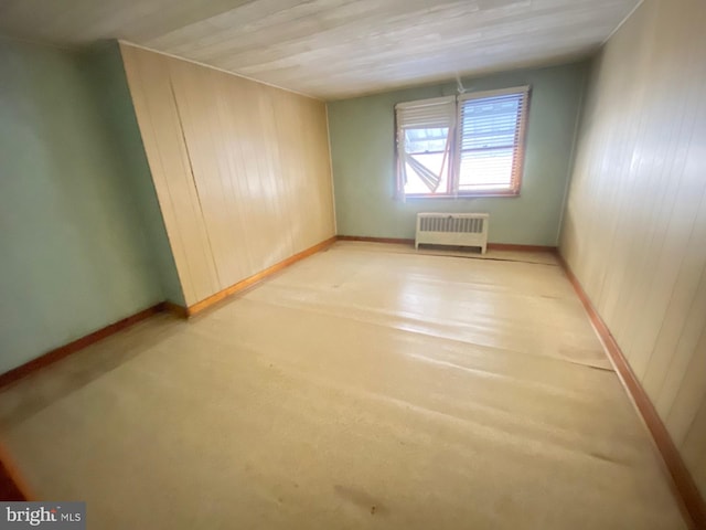 empty room featuring baseboards, wood walls, and radiator