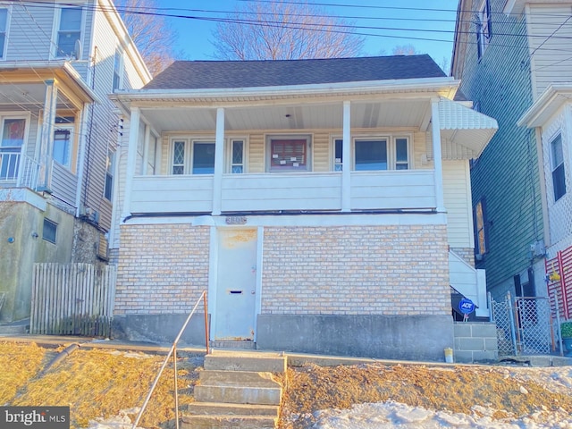 view of front of house with brick siding, roof with shingles, and fence