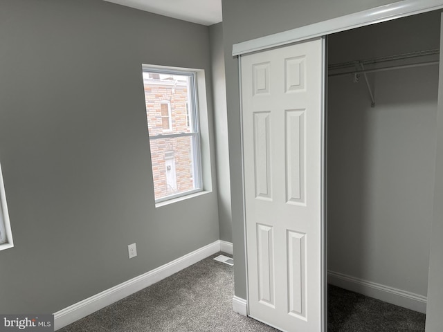 unfurnished bedroom with a closet, dark carpet, and baseboards