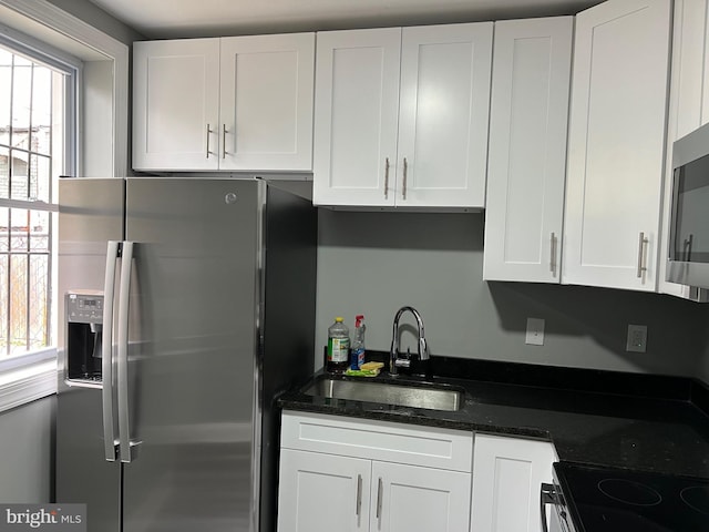 kitchen featuring appliances with stainless steel finishes, white cabinetry, a sink, and dark stone countertops