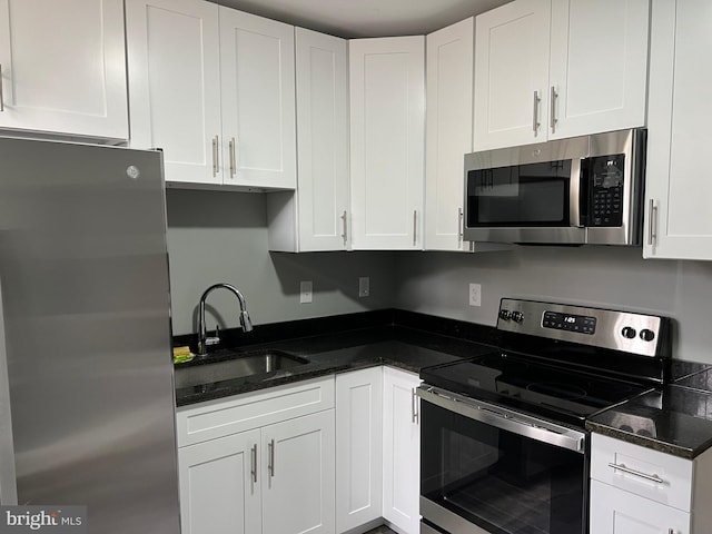 kitchen featuring appliances with stainless steel finishes, dark stone countertops, a sink, and white cabinets