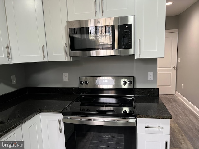 kitchen featuring baseboards, dark stone countertops, wood finished floors, stainless steel appliances, and white cabinetry